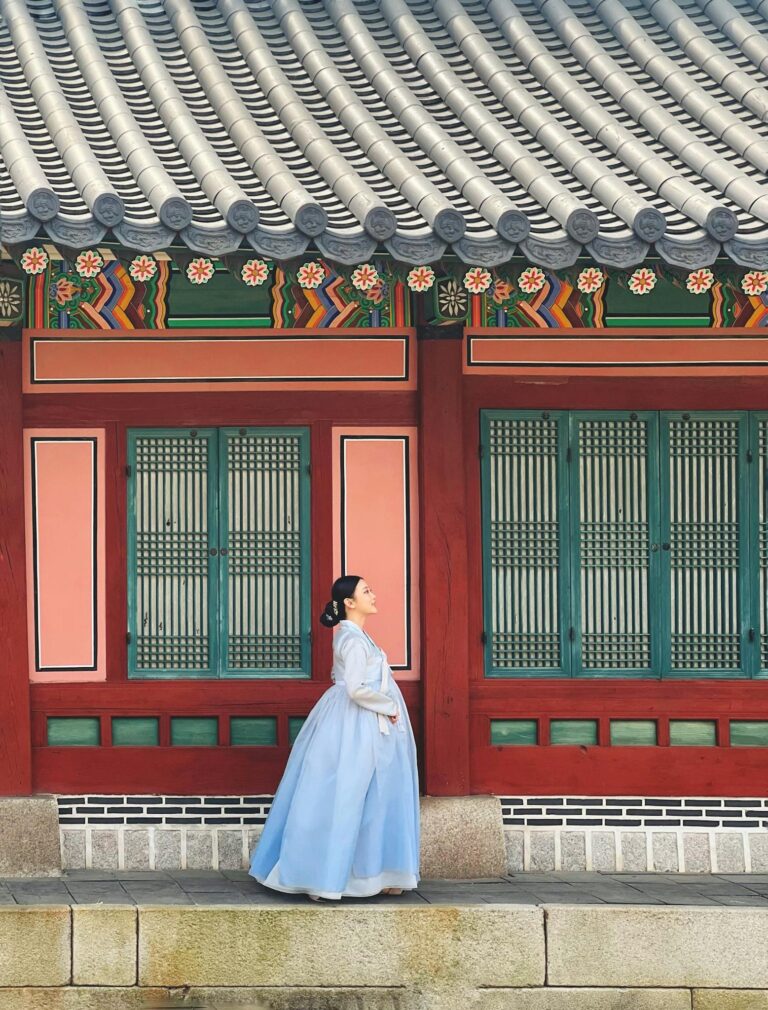 A woman in traditional Korean hanbok walks along Gyeongbokgung Palace's colorful architecture.